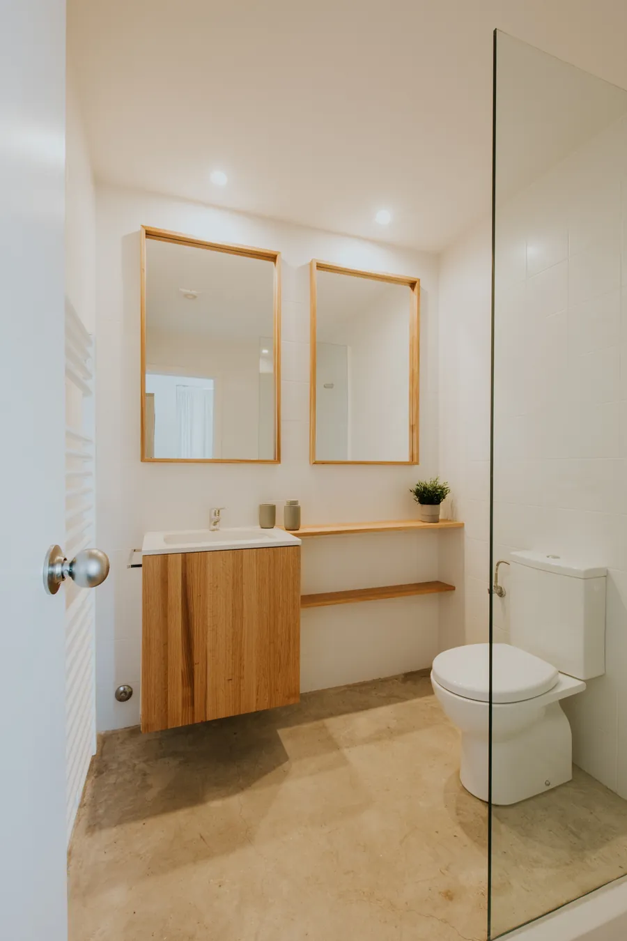 Baño con doble lavabo de madera, dos espejos y mampara de ducha