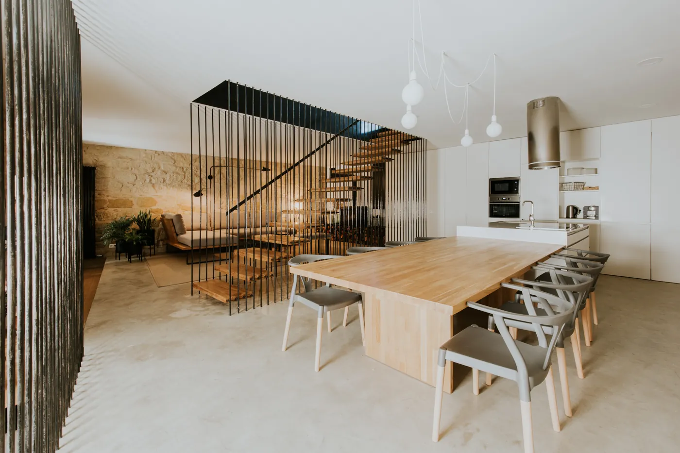 Cocina y comedor con una gran mesa de roble y la escalera flotante al fondo