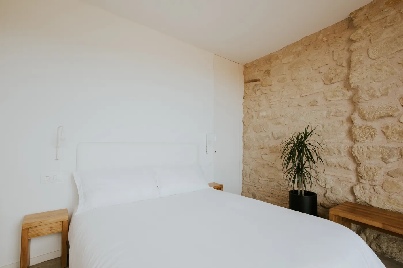 Habitación con cama de matrimonio, cabecero blanco y pared de piedra
