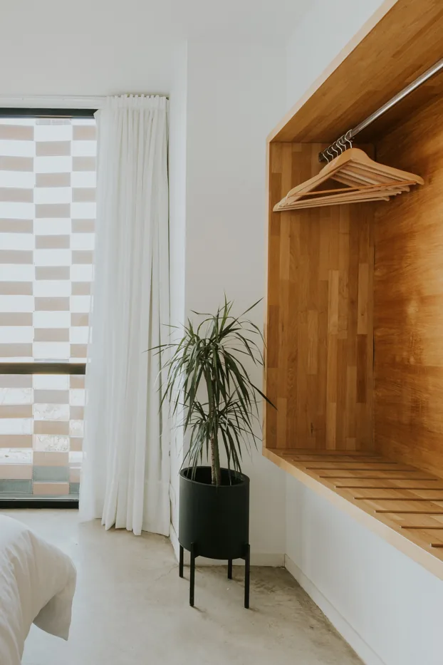 Rincón de una habitación con armario de roble, cortina blanca y una planta junto a la ventana